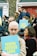 A group of people gathered outside with signs that read 'TRUTH JUSTICE LOVE' in bold yellow letters on a blue background. The crowd includes a diverse mix of individuals, some holding cameras, with expressions ranging from focused to contemplative. The background features red and blue doors with brick walls.
