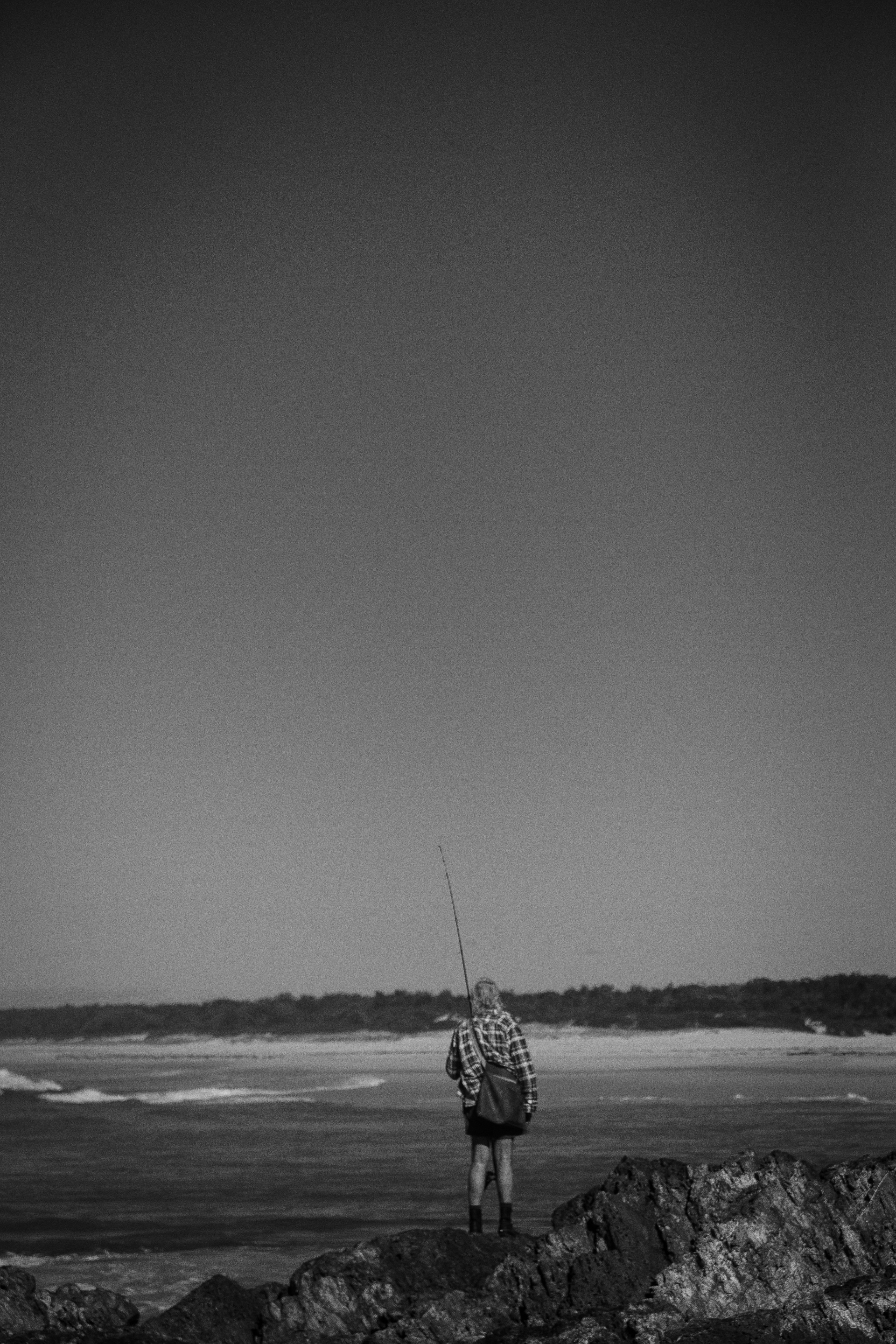 a man standing on top of a beach holding a fishing pole