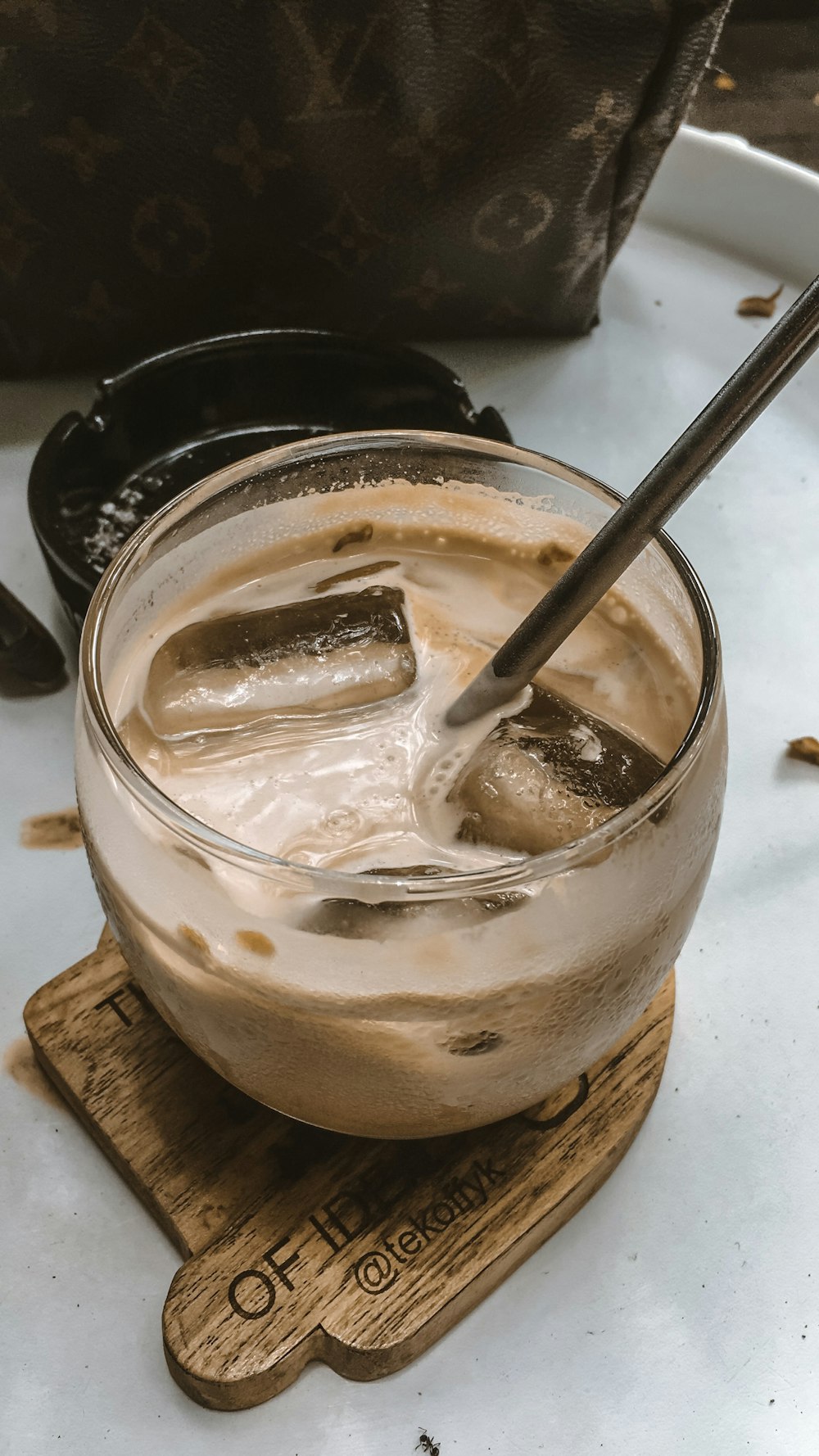 coffee with ice in clear glass near round black ceramic ashtray