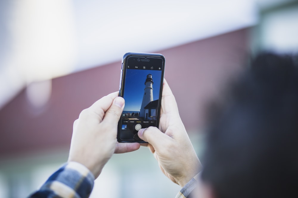 person taking photo of white and black lighthouse