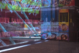 A colorful amusement park ride with vibrant paintings of cartoon characters and bright lights. The ride is enclosed with a white railing. Reflections and light streaks add an otherworldly effect to the scene.