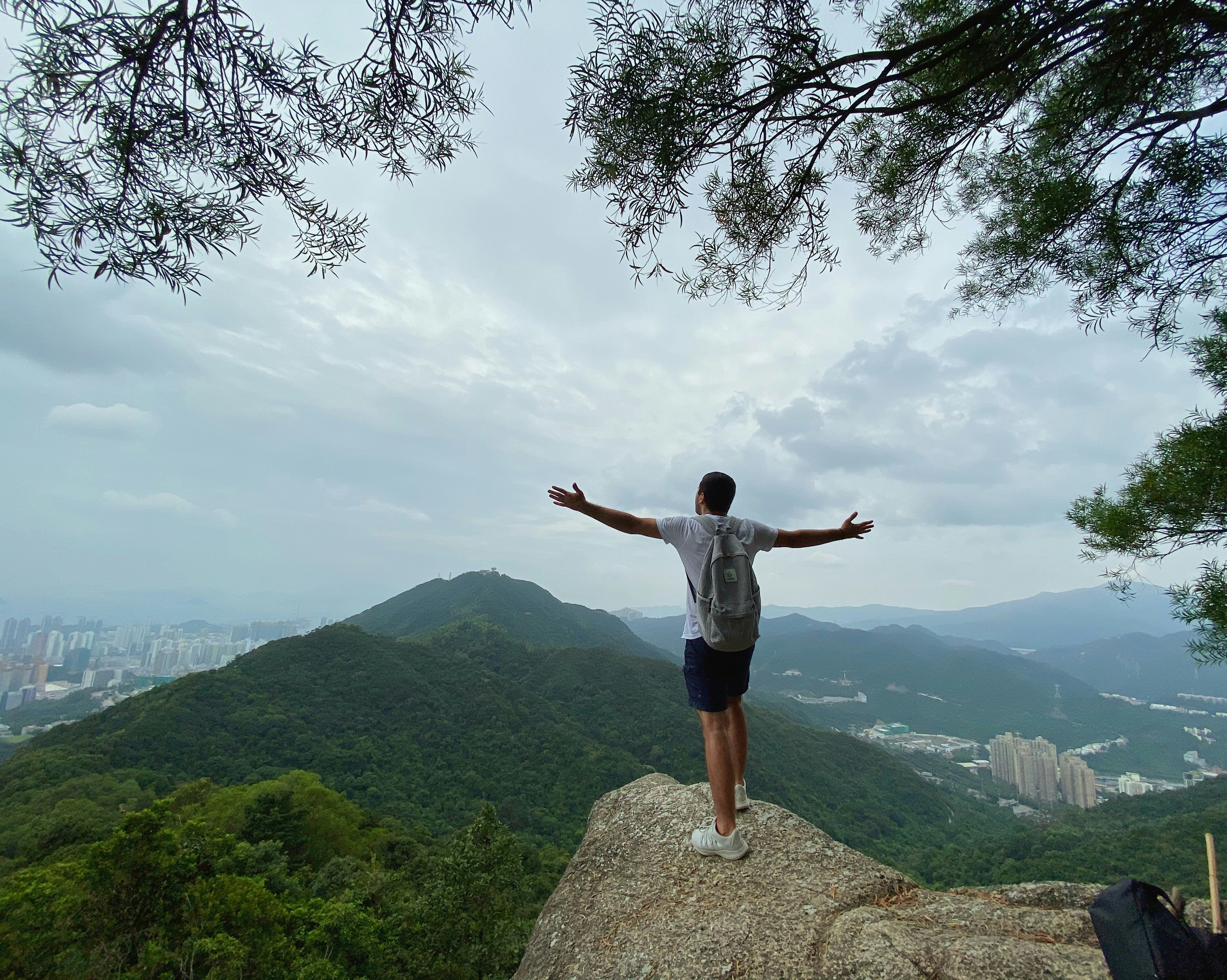 homme portant une chemise grise debout sur le bord du rocher regardant la montagne