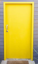 A locksmith unlocking a modern door with a bright yellow uniform in a residential neighborhood.