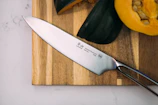 Close-up of a sleek stainless steel chef's knife resting on a wooden cutting board with fresh vegetables around.