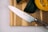 A sharp kitchen knife with a shiny blade and a metallic handle is placed on a wooden cutting board. Beside it, there are sliced and whole squash, showcasing their orange and green outer skins.