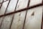 A series of weathered and cracked window panes, held together by a rusty metal framework. The glass has chicken wire embedded within, and some areas show significant damage with holes and missing fragments.