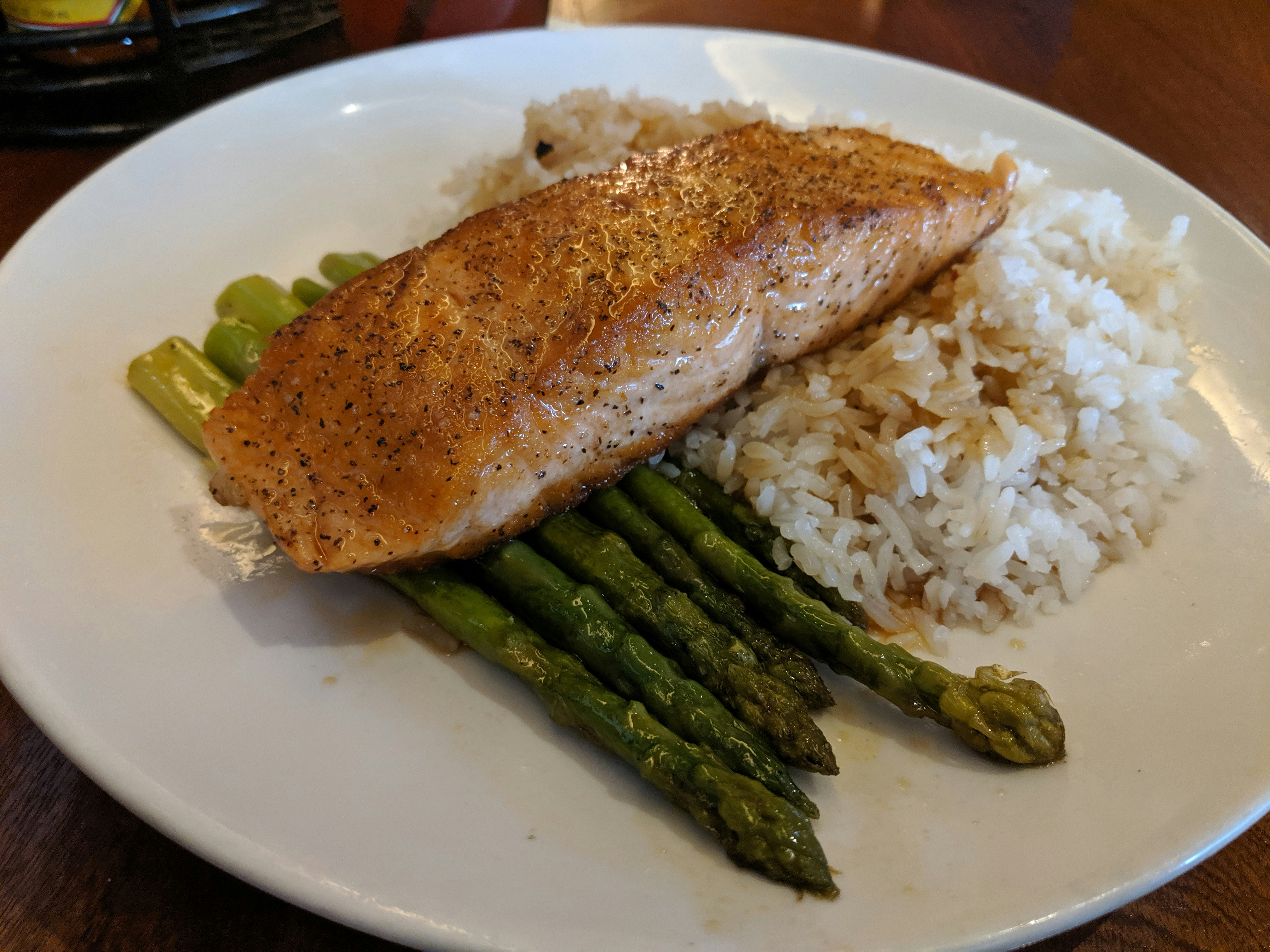 Perfectly baked salmon fillet next to roasted asparagus spears and cubes of roasted sweet potato in a meal prep container.