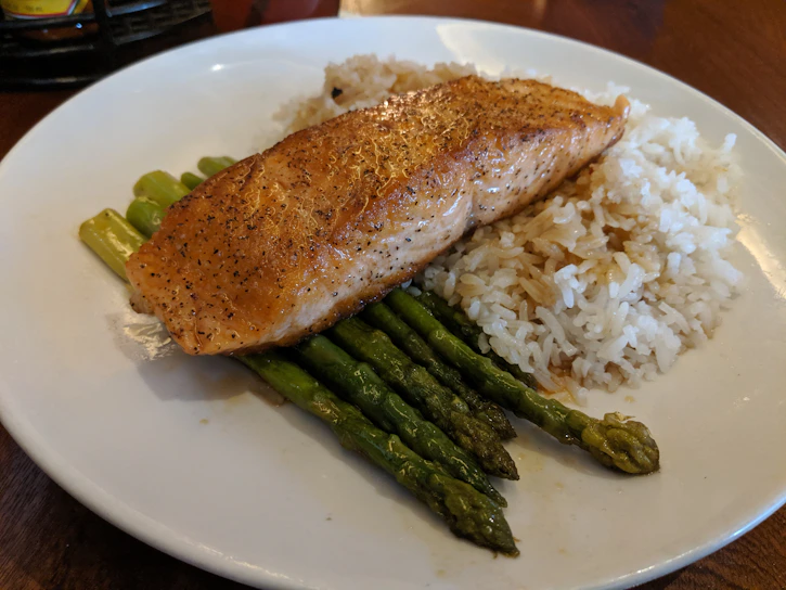 A close-up of a vibrant plate featuring golden ginger-glazed salmon with a side of steamed jasmine rice and fresh greens.