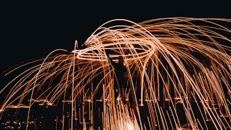 A dynamic display of bright, fiery orange sparks flying in circular patterns against a dark background, creating an eye-catching light painting effect.