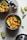 A colorful salsa made with chopped mangoes, red onions, red bell peppers, and cilantro, garnished with lime wedges and placed in a stainless steel container with its lid partially open. Another container sits next to it and additional lime wedges and cilantro leaves are scattered around.