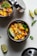 A colorful salsa made with chopped mangoes, red onions, red bell peppers, and cilantro, garnished with lime wedges and placed in a stainless steel container with its lid partially open. Another container sits next to it and additional lime wedges and cilantro leaves are scattered around.