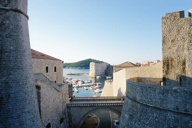 The Old Port of Dubrovnik seen through the stone city walls near the Ploce Gate, with boats moored inside the harbor