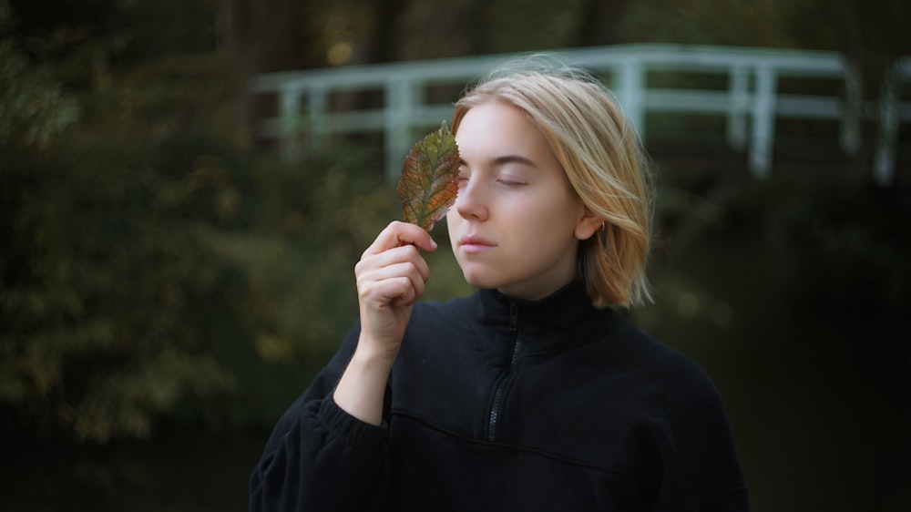 woman wearing black jacket holding brown leaf