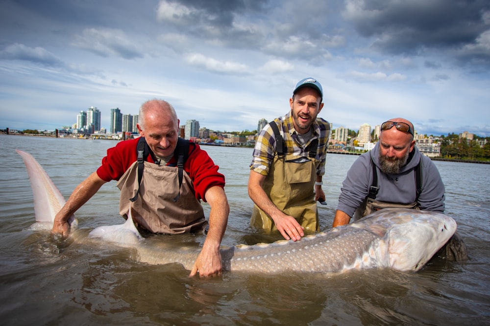 three men holding fish during day