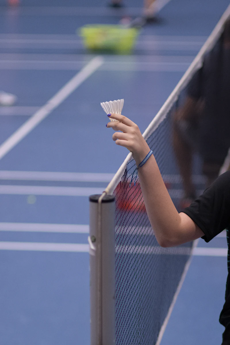 Badminton player holding a shuttlecock at the net on an indoor court