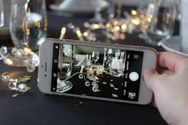 A smartphone held in a hand captures a close-up scene featuring elegantly arranged glassware with sparkling gems and lights in the background. The focus on the phone screen highlights the intricate details of the setup.