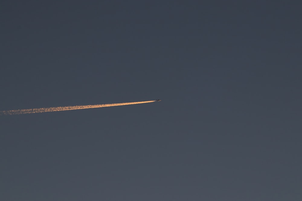 a jet flying through a blue sky with a contrail