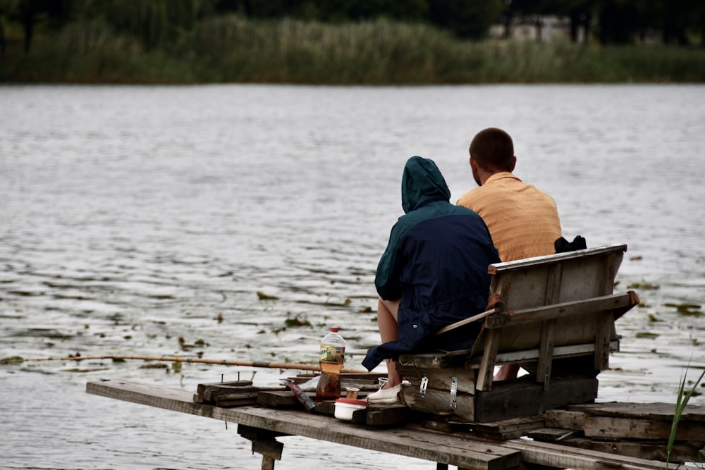 man and woman sitting on wooden chair in front of body of water