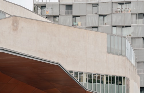An urban architectural scene featuring a modern building with geometric shapes and patterns. The structure includes large glass windows and metal siding, with balconies on one side. The image captures a section of the building with a blend of concrete and glass materials.