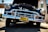 A classic vintage car with a shiny chrome grille and headlights is parked in an outdoor setting. The car's hood is open, displaying some of the engine components. The license plate reads 'California' and the scene is lit by bright sunlight, highlighting the reflective surfaces of the car.