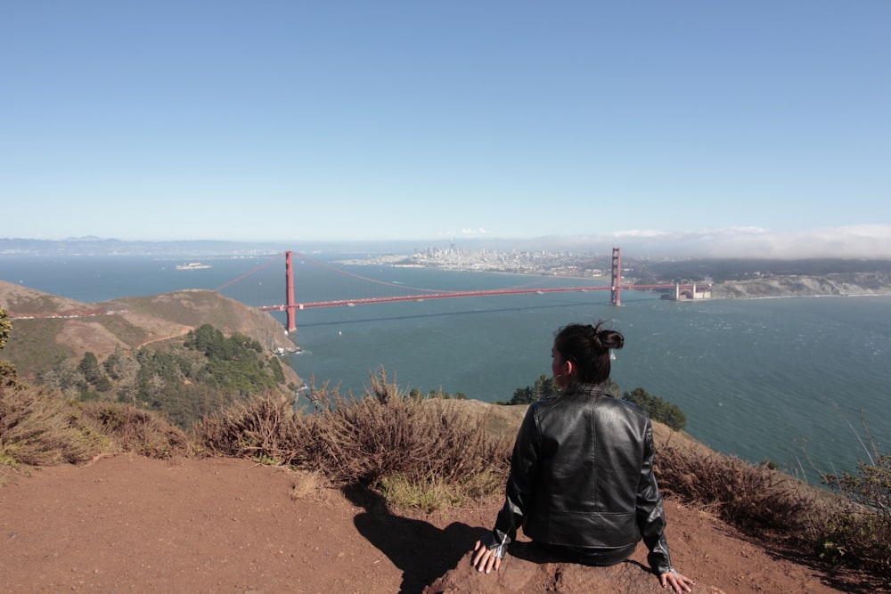 sitting woman facing body of water during daytime