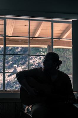 A quiet moment of Álvaro reflecting with his guitar by a window at sunset.