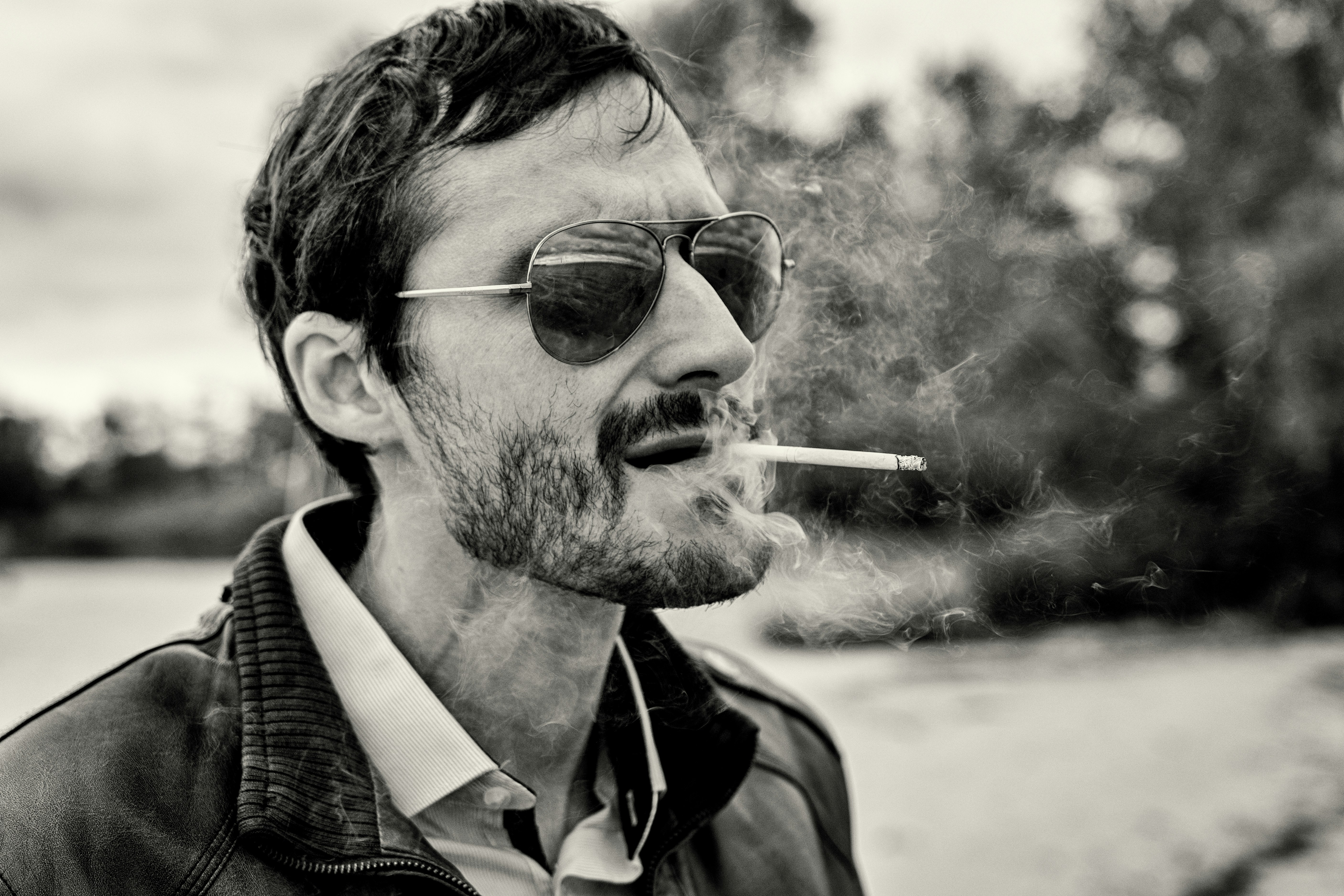 Ein Mann mit Sonnenbrille und Lederjacke, der eine Zigarette raucht