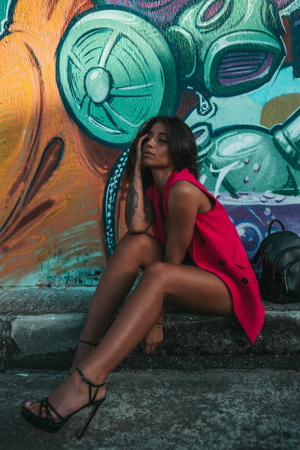 woman in red vest sitting on sidewalk with graffiti wall