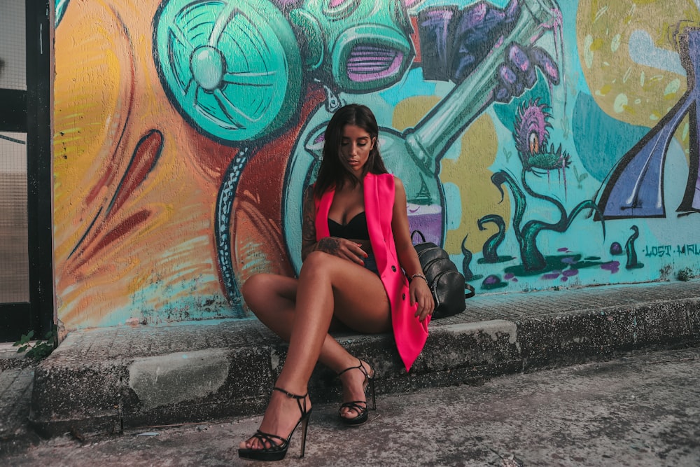 a woman sitting on the ground in front of a graffiti wall