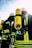 A group of firefighters wearing helmets and protective gear, including bright yellow oxygen tanks strapped to their backs. The reflective stripes on their suits are visible, and they seem to be preparing for or engaged in an operation outdoors under a clear sky.