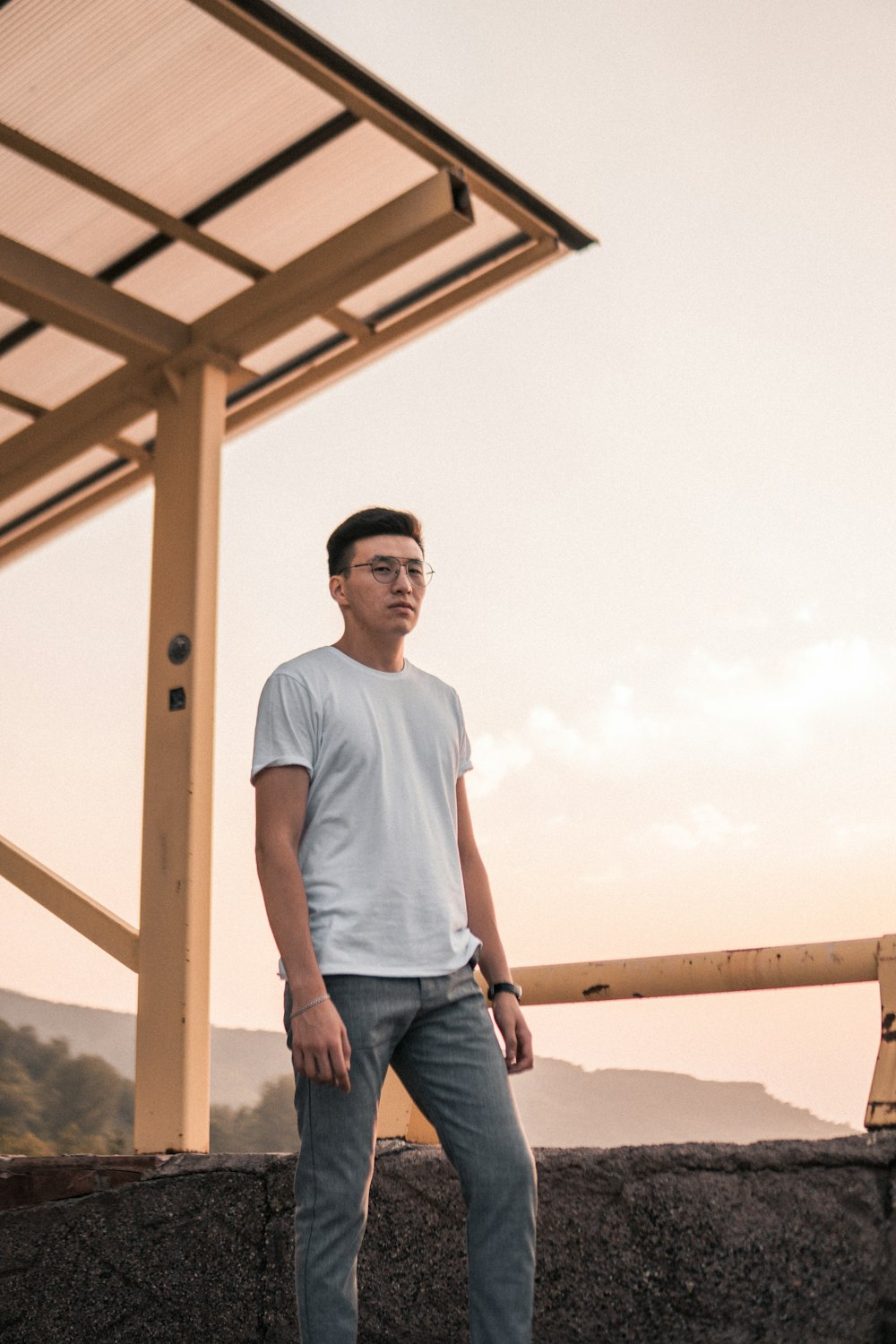 man wearing white crew-neck t-shirt and eyeglasses standing near pavement during daytime