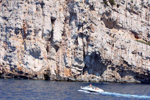A sleek modern RIB boat cruising near the rocky cliffs of Sella del Diavolo under a clear blue sky