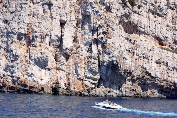 A sleek modern RIB boat cruising near the rocky cliffs of Sella del Diavolo under a clear blue sky.