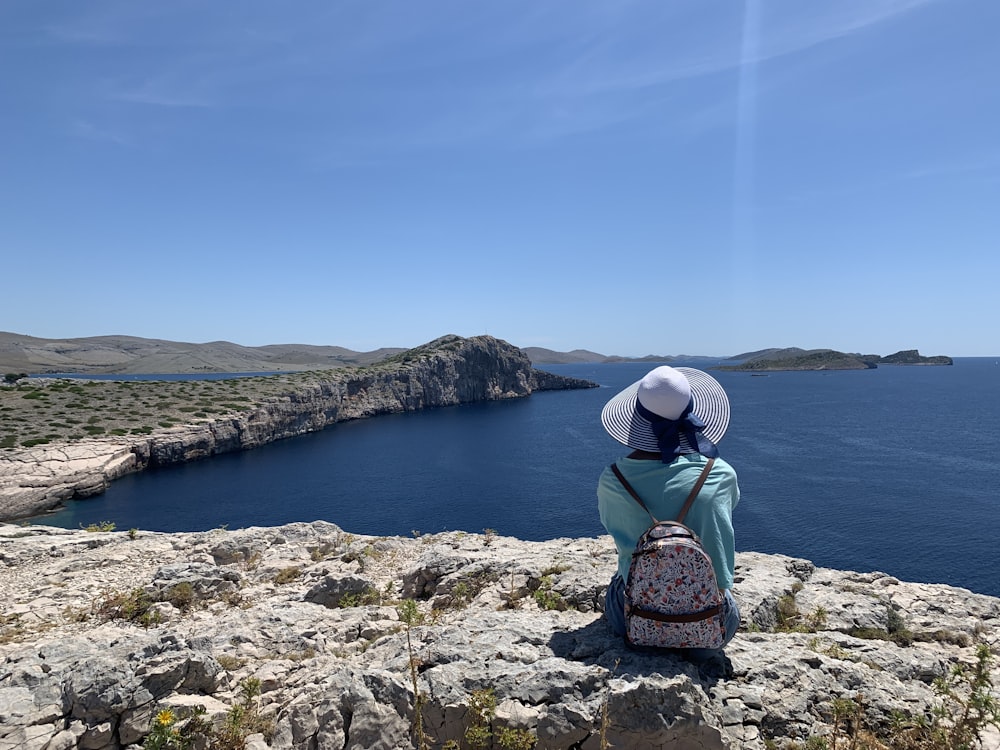 person wearing blue top and white hat sitting across body of water