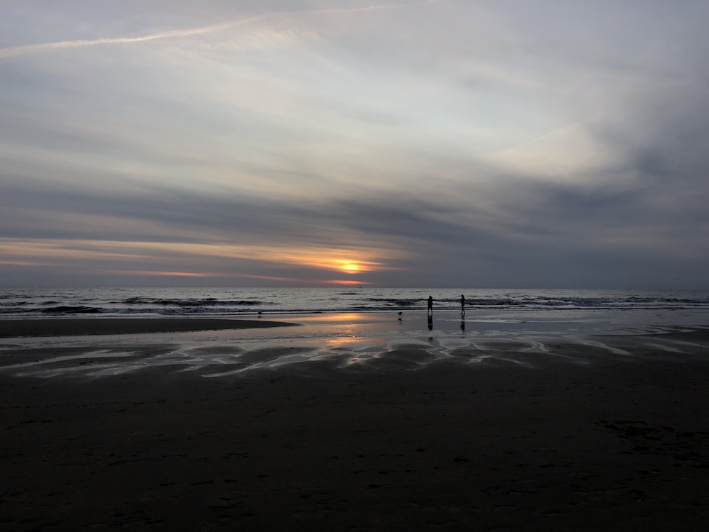 a couple of people standing on top of a beach under a cloudy sky