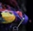 Two incense sticks emit delicate streams of smoke against a blurred, colorful background. The smoke swirls gracefully and creates a soft, ethereal atmosphere.