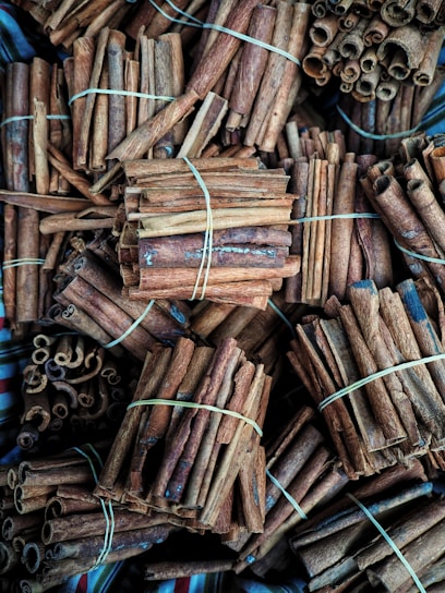 Bundles of cinnamon sticks tightly packed together, secured with elastic bands. The sticks vary in size and texture, with some curled and others straight, displaying a rich brown color.
