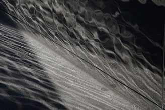 A textured surface with wavy, metallic reflections juxtaposed with a grainy, concrete-like texture. The lighting creates a contrast between shiny and matte areas, emphasizing the intricate patterns and lines.