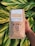 A hand holds a bag of Bixby Roasting Co. light roast coffee in front of large green leaves. The packaging is brown with blue and white designs, featuring a dog's face. Labels indicate the coffee is a mix from Kona, Colombia, and Costa Rica, and it is available as whole bean or ground.
