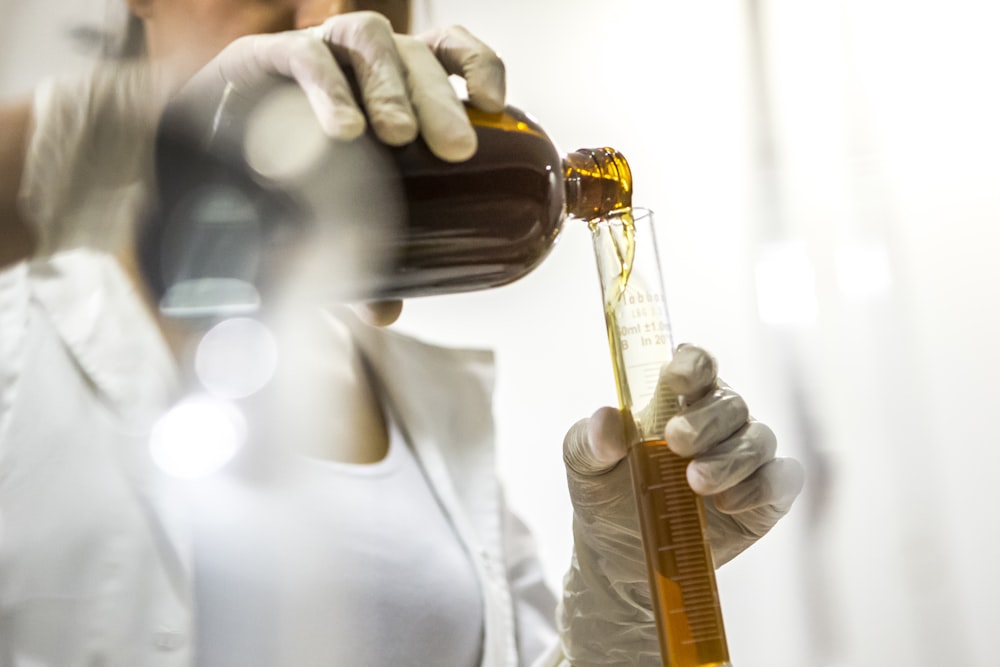 Femme portant une blouse blanche tenant une bouteille brune et un tube en verre