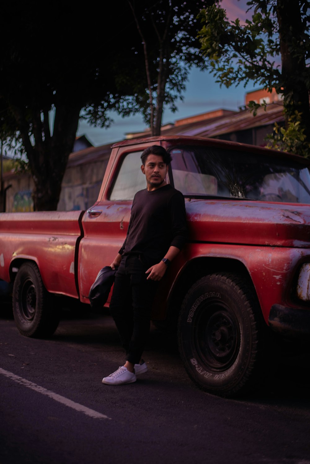 man in black shirt leaning on red pickup truck