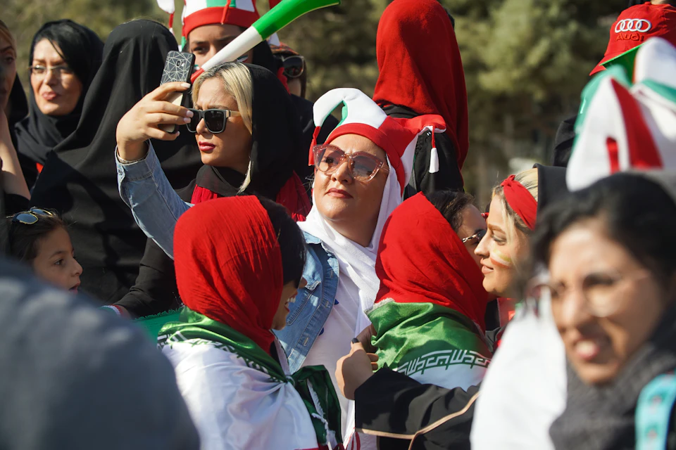 Large group of people gathered together wearing red and white headscarves taking selfies outdoors