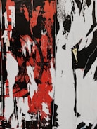 A chaotic and abstract composition featuring bold, distressed patterns in black, red, and white, with overlapping layers and vertical streaks. The forms suggest the remnants or peeling layers of street art or graffiti.