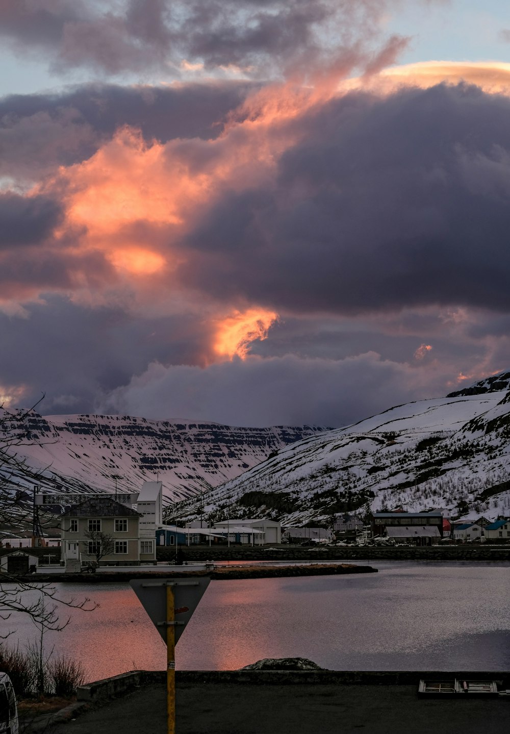 Casas cerca del cuerpo de agua con vista a la montaña cubierta de nieve bajo el cielo blanco y naranja