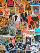 A collage of various vintage and modern music posters covering a wall. The posters feature bands and artists like Public Enemy, Guns N' Roses, The White Stripes, and others. The arrangement is vibrant, showcasing a variety of styles, colors, and typography.