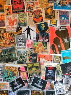 A collage of various vintage and modern music posters covering a wall. The posters feature bands and artists like Public Enemy, Guns N' Roses, The White Stripes, and others. The arrangement is vibrant, showcasing a variety of styles, colors, and typography.