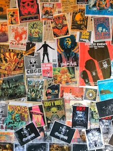 A collage of various vintage and modern music posters covering a wall. The posters feature bands and artists like Public Enemy, Guns N' Roses, The White Stripes, and others. The arrangement is vibrant, showcasing a variety of styles, colors, and typography.