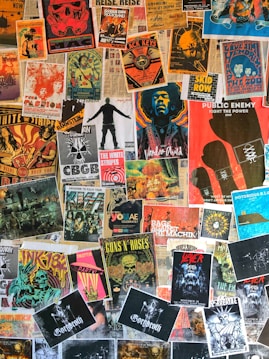 A collage of various vintage and modern music posters covering a wall. The posters feature bands and artists like Public Enemy, Guns N' Roses, The White Stripes, and others. The arrangement is vibrant, showcasing a variety of styles, colors, and typography.