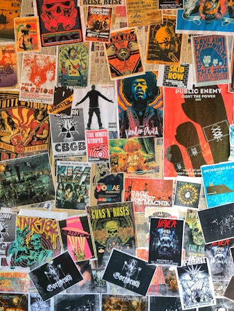 A collage of various vintage and modern music posters covering a wall. The posters feature bands and artists like Public Enemy, Guns N' Roses, The White Stripes, and others. The arrangement is vibrant, showcasing a variety of styles, colors, and typography.
