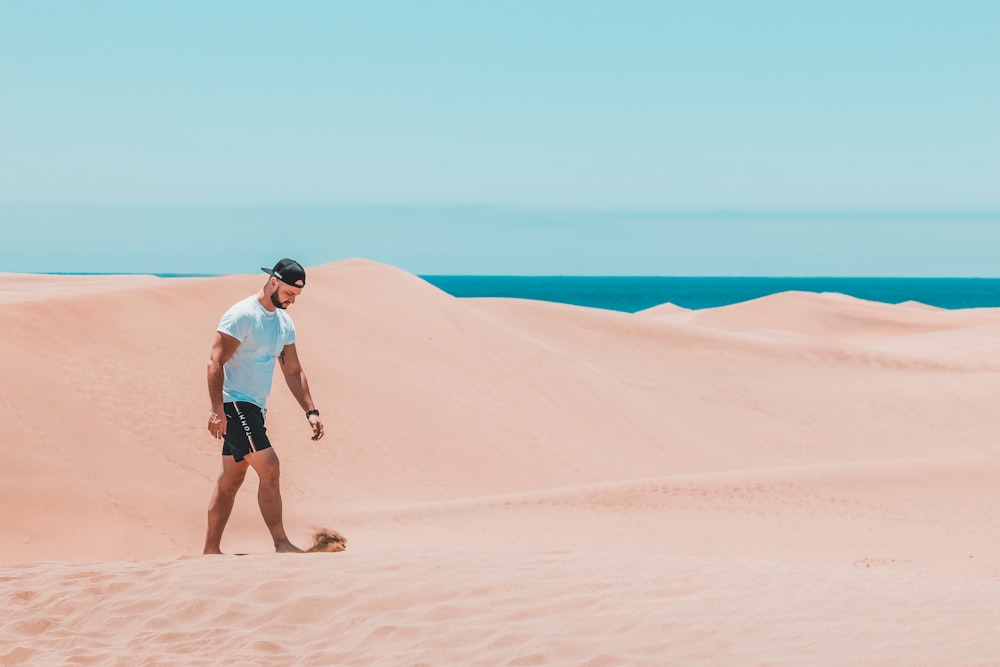 Mann trägt blaugrünes Hemd mit Rundhalsausschnitt und schwarze Shorts, die auf einer Sanddüne spazieren gehen